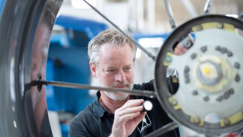 Mechaniker Marc Dietel inspiziert den Heckrotor eines Airbus H145 mithilfe einer Taschenlampe. Im Hintergrund sind verschwommen große Gerätschaften zu sehen.
