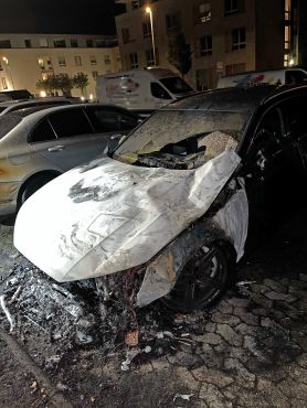 Ein ausgebranntes Auto steht auf einem Parkplatz.